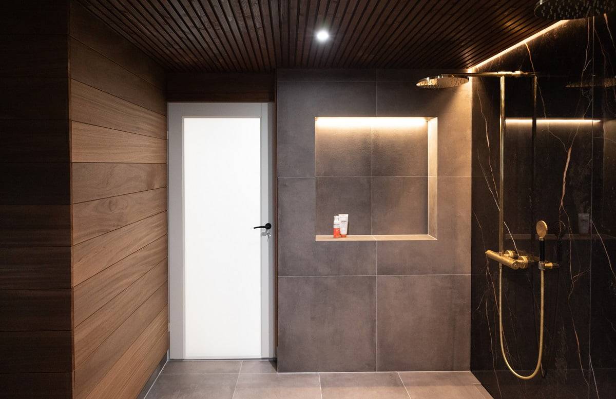 La tira de leds en la ranura del techo y en la parte superior del estante del champú proporcionan una suave luz ambiental en el cuarto de baño. Focos adicionales fijos y estancos de 9 W. © LedStore.fi
